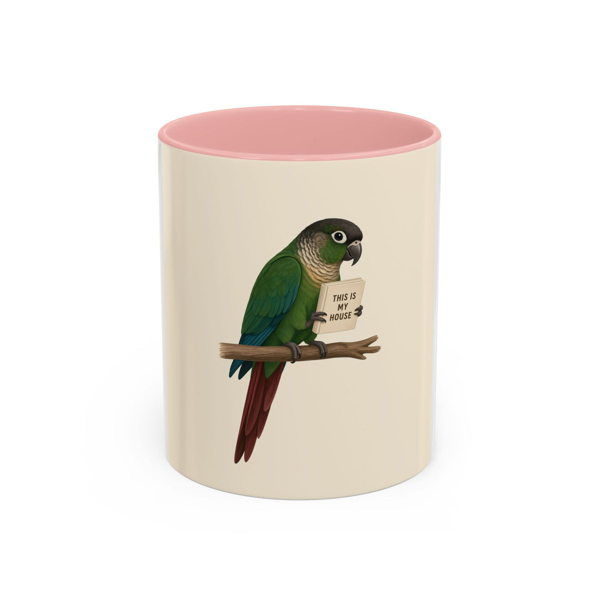 A ceramic mug with a white and cream-colored exterior and a pink interior, featuring a printed illustration of a green parrot perched on a branch holding a sign that reads 'THIS IS MY HOUSE'.
